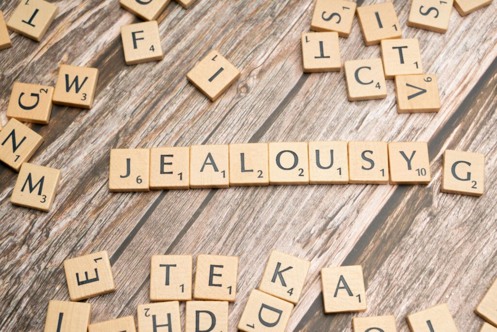 Wooden Scrabble letter tiles forming the word 'Jealousy' on a rustic wooden surface.