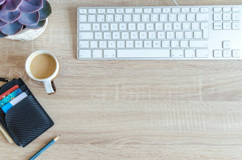 An organized workspace with a keyboard, coffee cup, wallet, and succulent plant on a wooden desk.