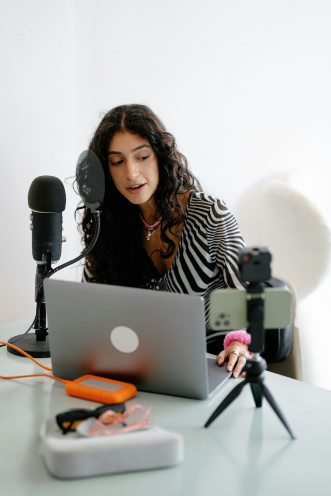 pexels photo 13929964 13929964 A young woman using a microphone and laptop to record a podcast indoors, showcasing a modern content creation setup.