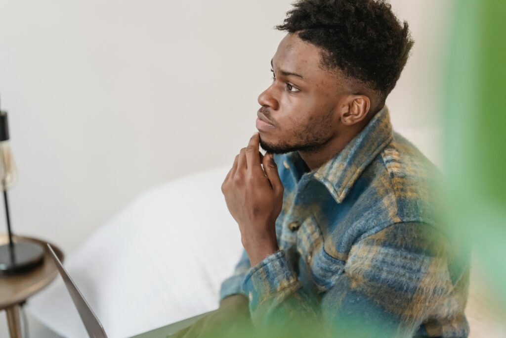 pexels photo 6578415 6578415 Pensive young man sitting indoors, touching chin, in a peaceful setting, deeply focused.