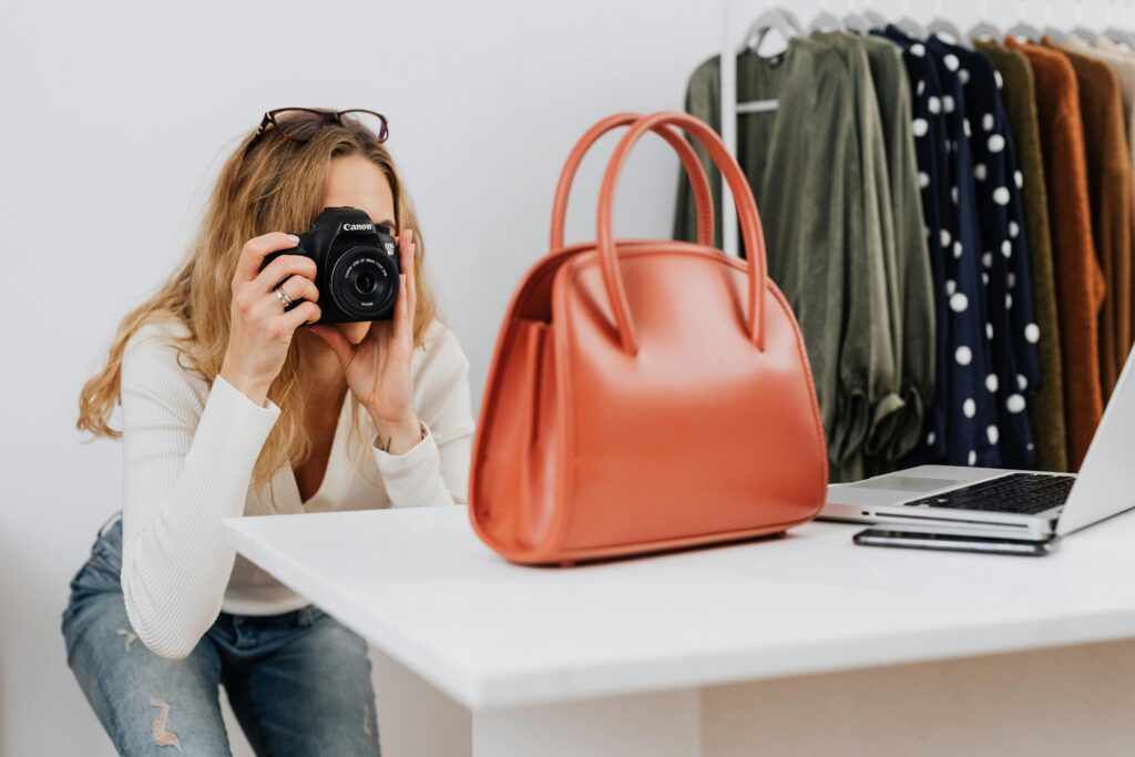 Caucasian woman capturing handbag photos for online fashion retail with camera.