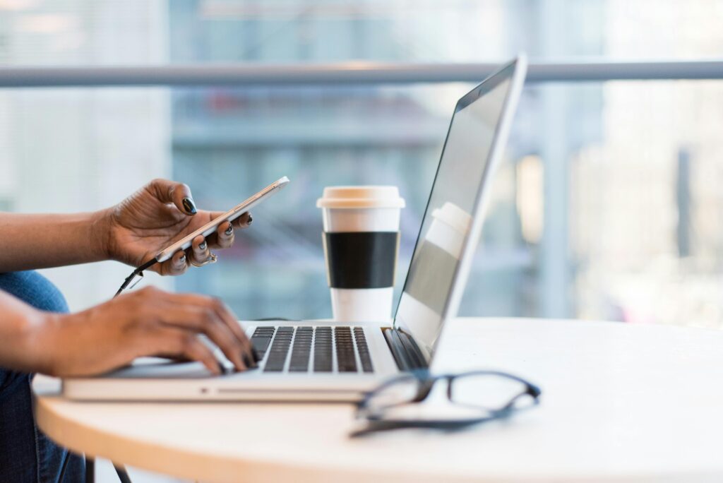 pexels photo 1181248 1181248 Close-up of hands using a laptop and phone with coffee on a modern office desk.