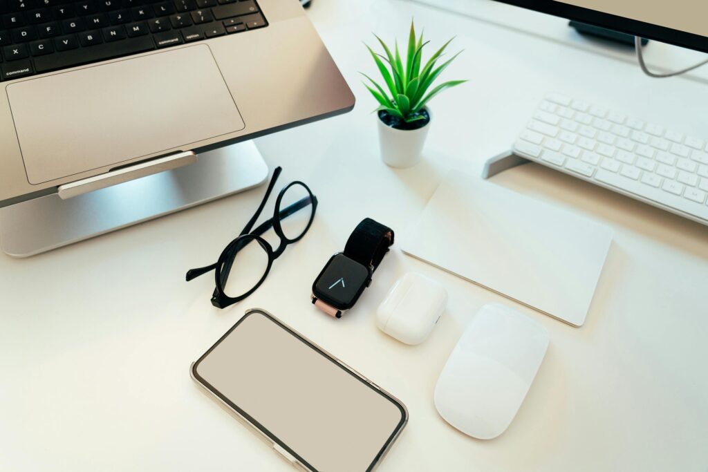 Overhead view of a sleek workspace with a laptop, smartphone, smartwatch, and tech accessories.