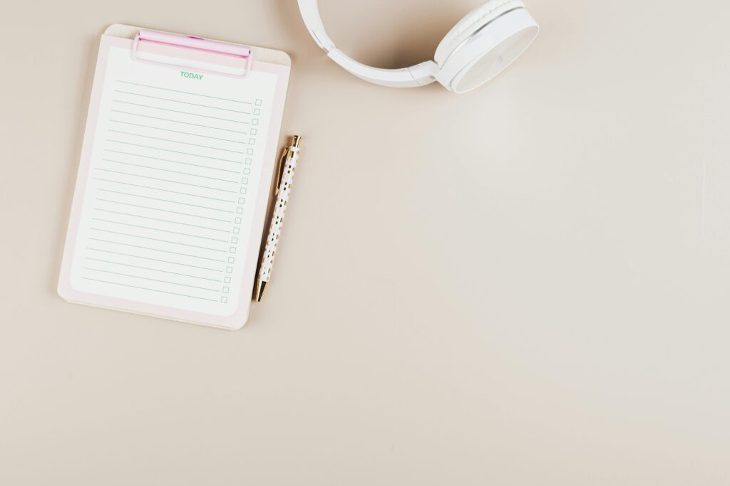 A simplistic flat lay of a notepad, pen, and headphones on a white background.