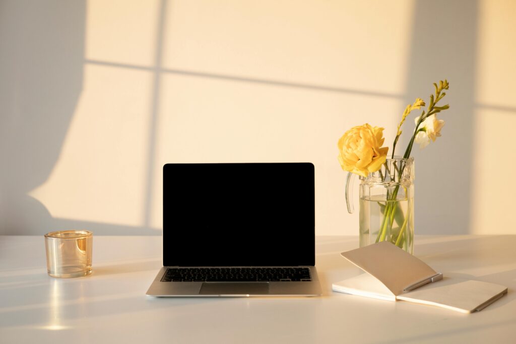 A serene minimalist workspace featuring a laptop, flowers, and a notebook, ideal for productivity and creativity.